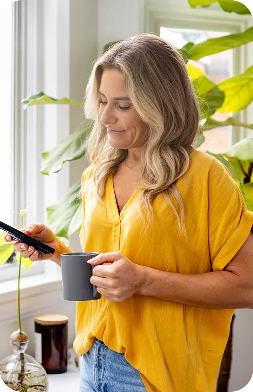Happy woman at home looking at social media on her cell phone while drinking a cup of coffee - lifestyle concepts